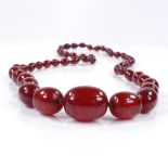 A string of graduated cherry red amber beads, containing 53 beads, largest measures 26.3mm x 20.7mm,