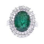 An 18ct white gold emerald and diamond cluster cocktail ring, with diamond set shoulders, oval-cut