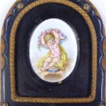 A 19th century painted porcelain plaque depicting a cherub, in original brass-mounted ebonised
