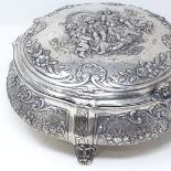 A large German circular silver box, with hinged lid, on scrolled acanthus leaf feet, relief embossed