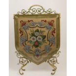 Victorian brass and tapestry firescreen, shield shaped panel worked in gross-point, with a floral