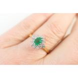 Emerald and diamond cluster ring, the oval cut emerald of approx. 0.25ct bordered with 14 small