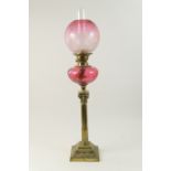 Edwardian brass and cranberry glass pedestal oil lamp, the globular shade etched with flowers in Art