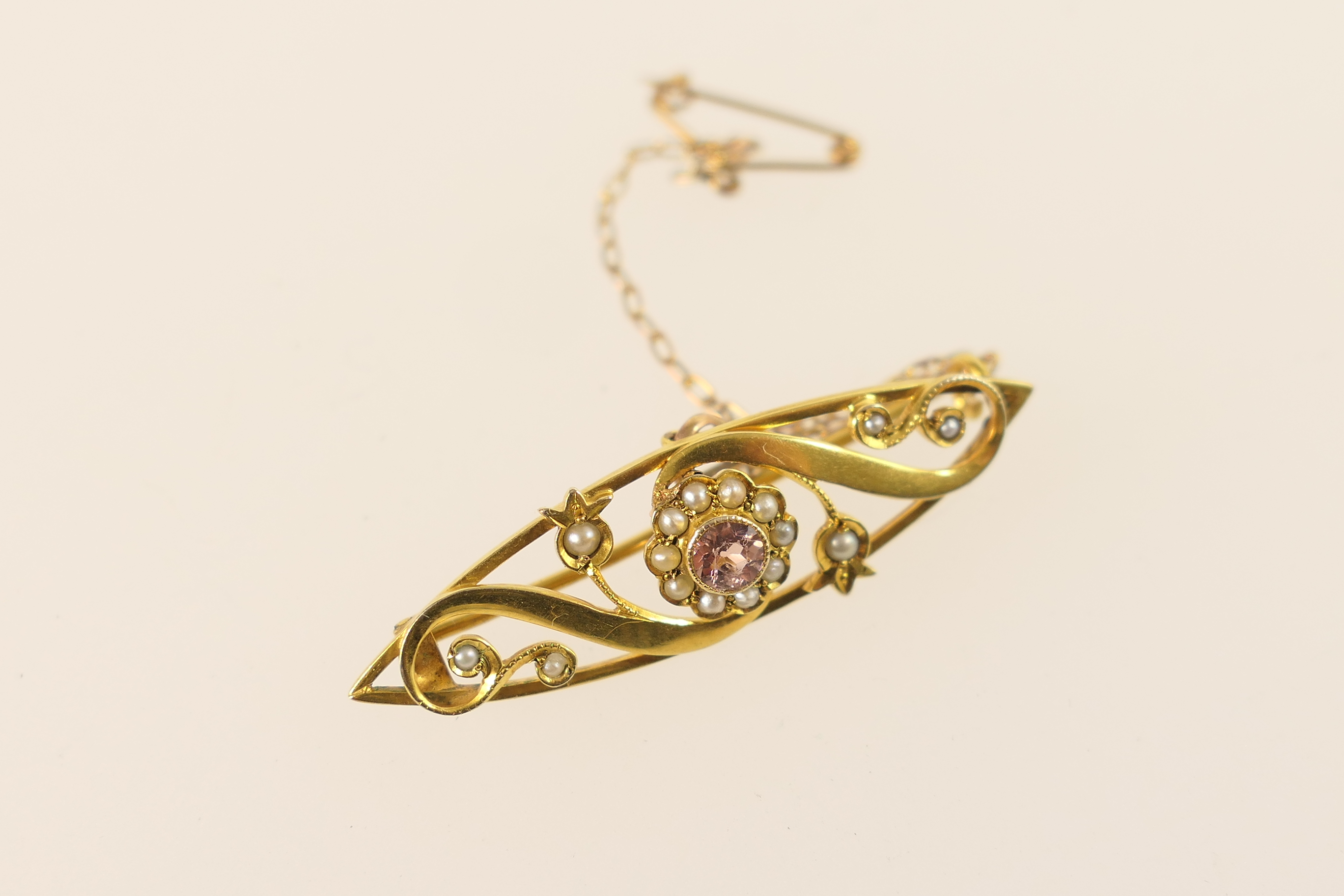 Edwardian 9ct gold bar brooch, the navette open scroll form centred with a pink tourmaline