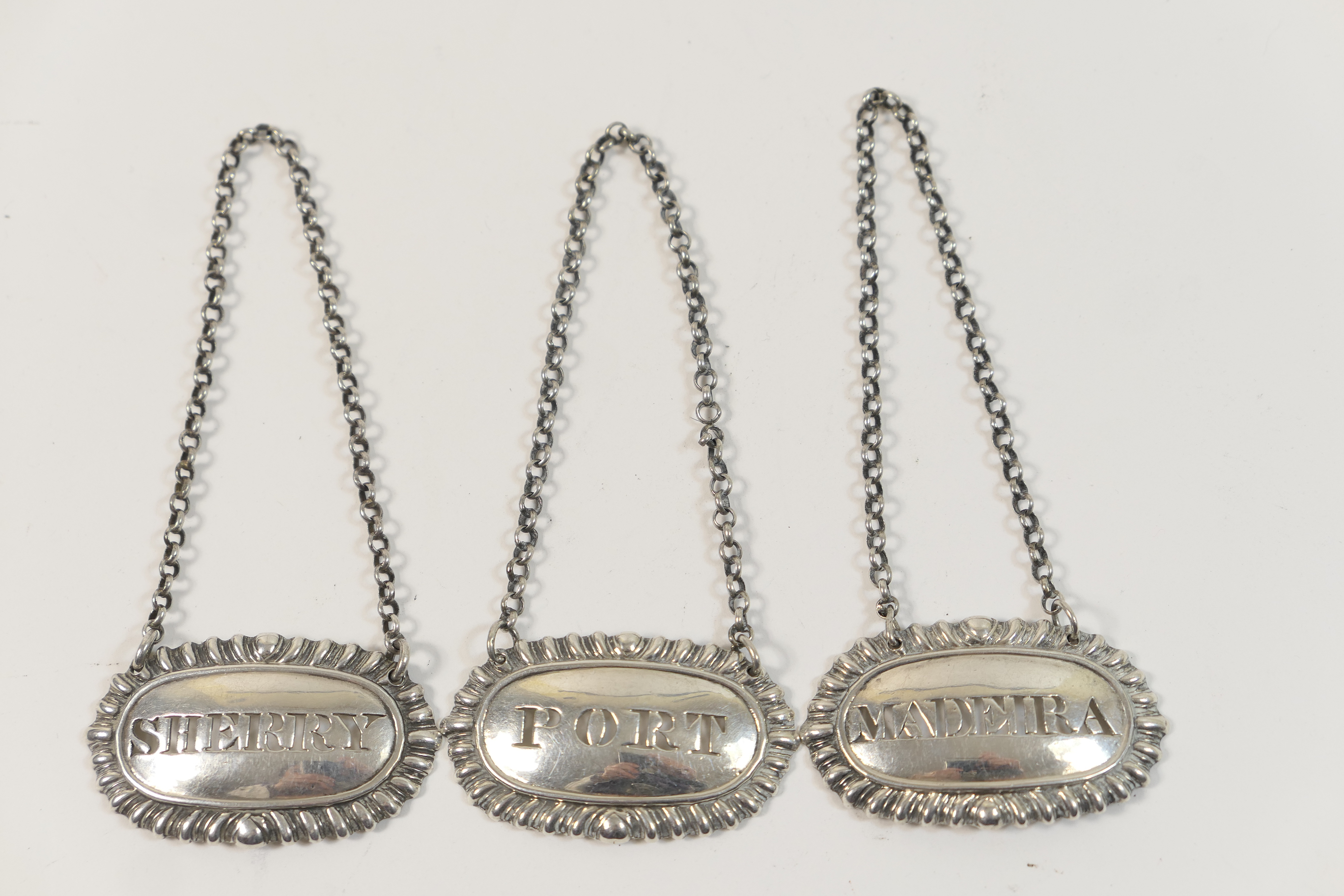 Three Victorian silver decanter labels, each of oval form with gadrooned edge, pierced with '