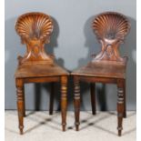 A pair of George IIII mahogany hall chairs with carved oval shell and scroll backs, wood seats on