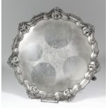 An Edward VII silver circular salver, the shaped and moulded rim with leaf scroll mounts, the centre