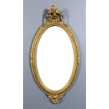A gilt framed oval wall mirror with floral and vine cresting, the frame moulded with leaf scroll