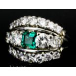 A modern silvery coloured metal mounted diamond and emerald ring, the central emerald (approximately