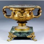 A late 19th Century gilt metal two-handled urn of Roman form, modelled with male heads, on green