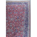 A Tabriz carpet woven in colours with a bold leaf and trailing floral palmettes design on a dark red