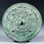 An early Chinese archaic patinated tinned bronze circular mirror, the plain silvered face with green
