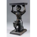 A late 19th/early 20th Century ebonised wood table card tray carved as a kneeling figure holding a