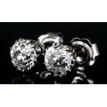 A pair of silvery metal mounted solitaire diamond earrings (for pierced ears), each set with