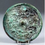 An early Chinese archaic patinated bronze circular mirror with plain face, the reverse cast in