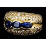 A modern French 18ct gold mounted sapphire and diamond bombe pattern ring, the face set with three