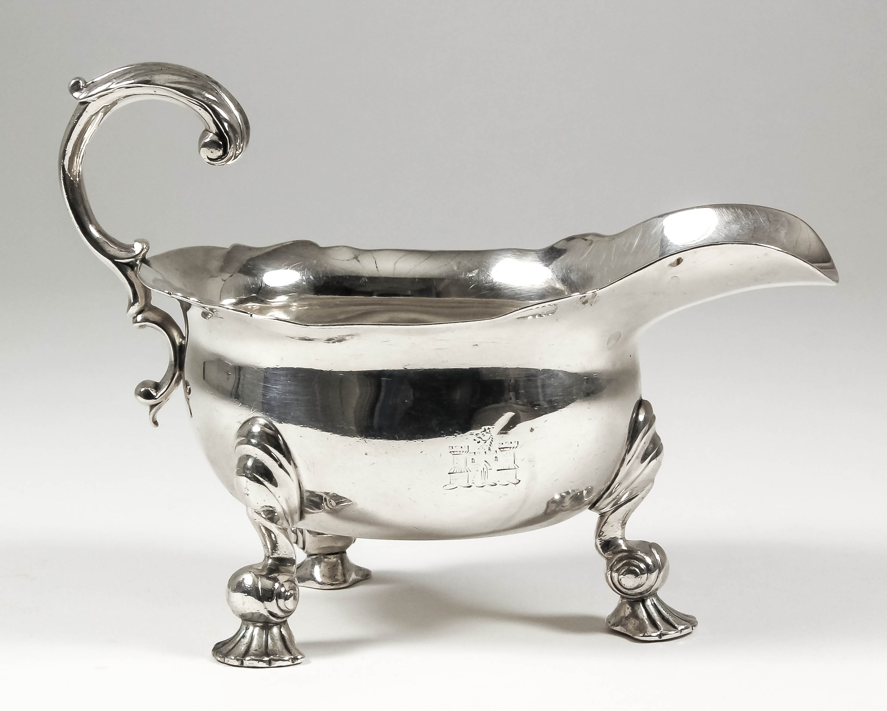 A good George II cast silver oval sauce boat with shaped rim and leaf capped flying scroll handle,