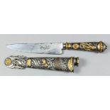 An Argentinian silvery metal and gilt metal goucho knife and scabbard, embossed with figures and