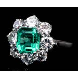 A silvery coloured metal mounted emerald and diamond cluster ring, set with central rectangular