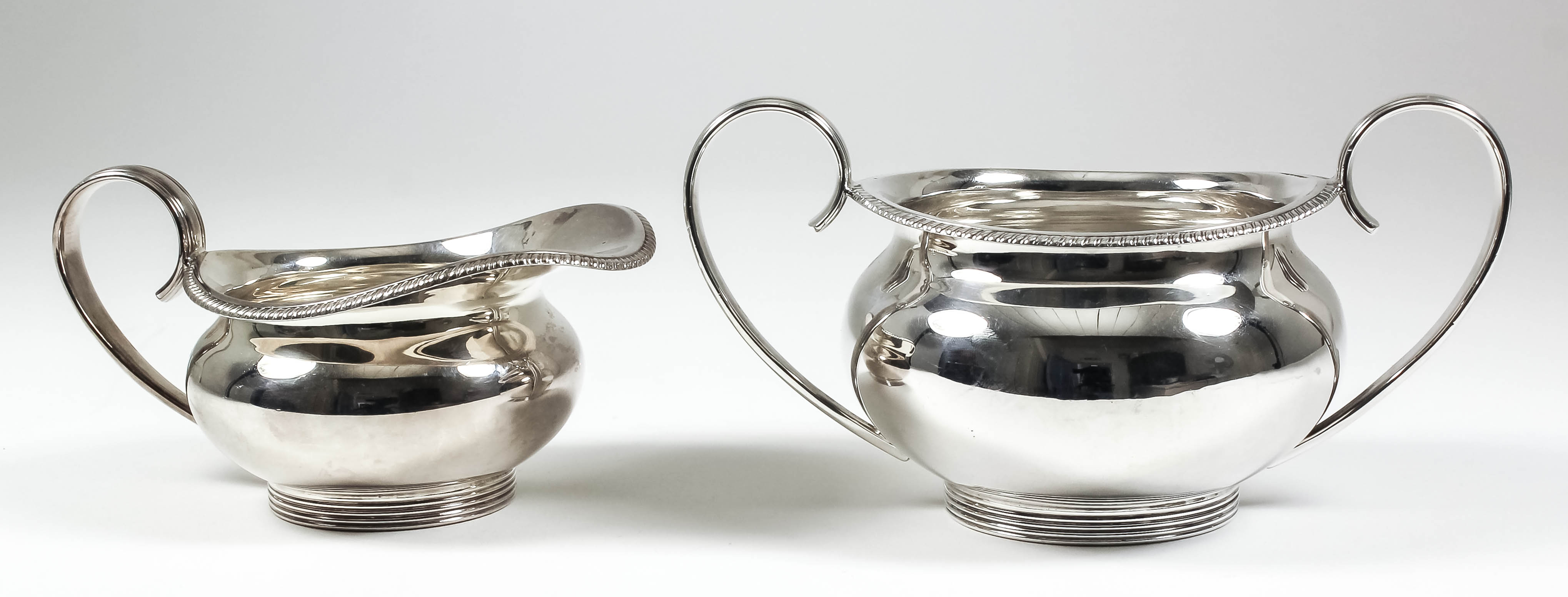 A George V silver circular two-handled sugar basin and matching milk jug, the bulbous bodies with