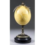 A carved ostrich egg, mounted on a plated metal stand and ebonised base, 11.5ins high