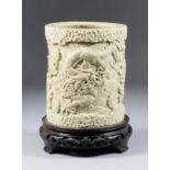 A Chinese cream glazed stoneware brush pot moulded with dragons above waves, with carp, 4.75ins (
