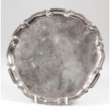 A late Victorian silver circular salver with shaped and moulded rim, on three scroll feet, 9ins