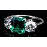 A silvery coloured metal mounted three stone emerald and diamond ring, set with central octagonal