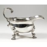 A George II cast silver oval sauce boat with shaped rim and leaf capped flying scroll handle, on