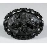 A black composition mounted oval brooch, inset with "jet" panel carved with flowers and leaves, 51mm