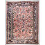 A Kirman carpet woven in colours with bold floral motifs on a rose ground within floral filled seven