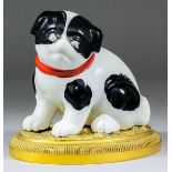 An unusual Japanese porcelain figure of a black and white puppy with red ribbon around its neck,