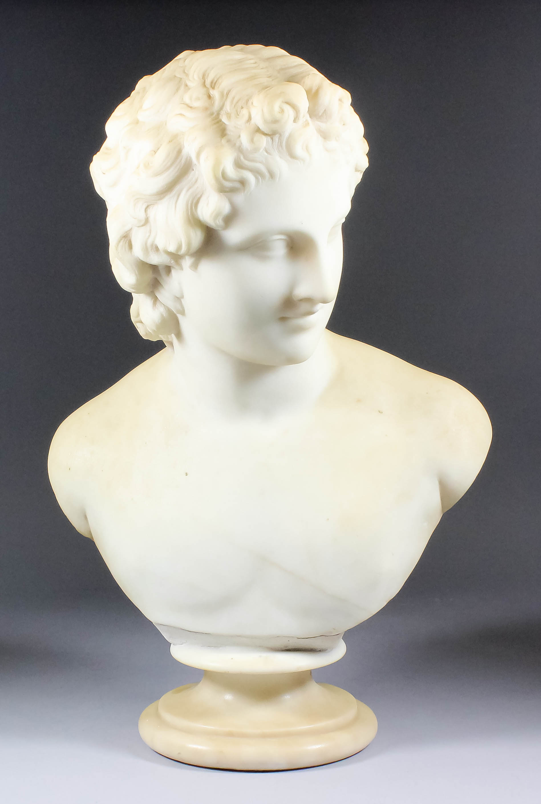 A 19th Century white marble bust of a young man, possibly Apollo, on circular socle, 20ins high