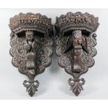 A pair of Asian hardwood wall brackets of shaped outline, carved and fretted with leaf and floral