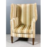 An early 20th Century wingback easy chair, upholstered in striped cloth, on square tapered front