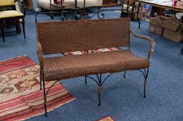 A LATE NINETEENTH CENTURY BLACK WROUGHT IRON WIRE PATTERN TWO SEATER SETTEE with woven cane back,