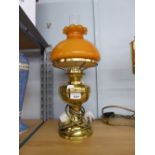 AN ADAPTED OIL LAMP WITH ORANGE GLASS GLOBE AND CLEAR GLASS FUNNEL