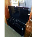 A SAMSUNG 40" FLAT SCREEN TELEVISION, ON BLACK GLASS THREE TIER STAND