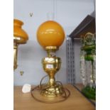 AN ADAPTED OIL LAMP WITH ORANGE GLASS GLOBE AND CLEAR GLASS FUNNEL