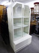 A MODERN WHITE DISPLAY CABINET, WITH INTERNAL LIGHT, OVER BASE HAVING ONE DRAWER