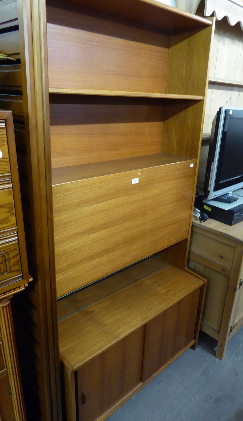 A TEAK NARROW WALL UNIT WITH DROP-FRONT SECTION TO THE TOP AND SLIDING DOORS BELOW