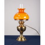 AN ADAPTED OIL LAMP WITH ORANGE GLASS GLOBE AND CLEAR GLASS FUNNEL