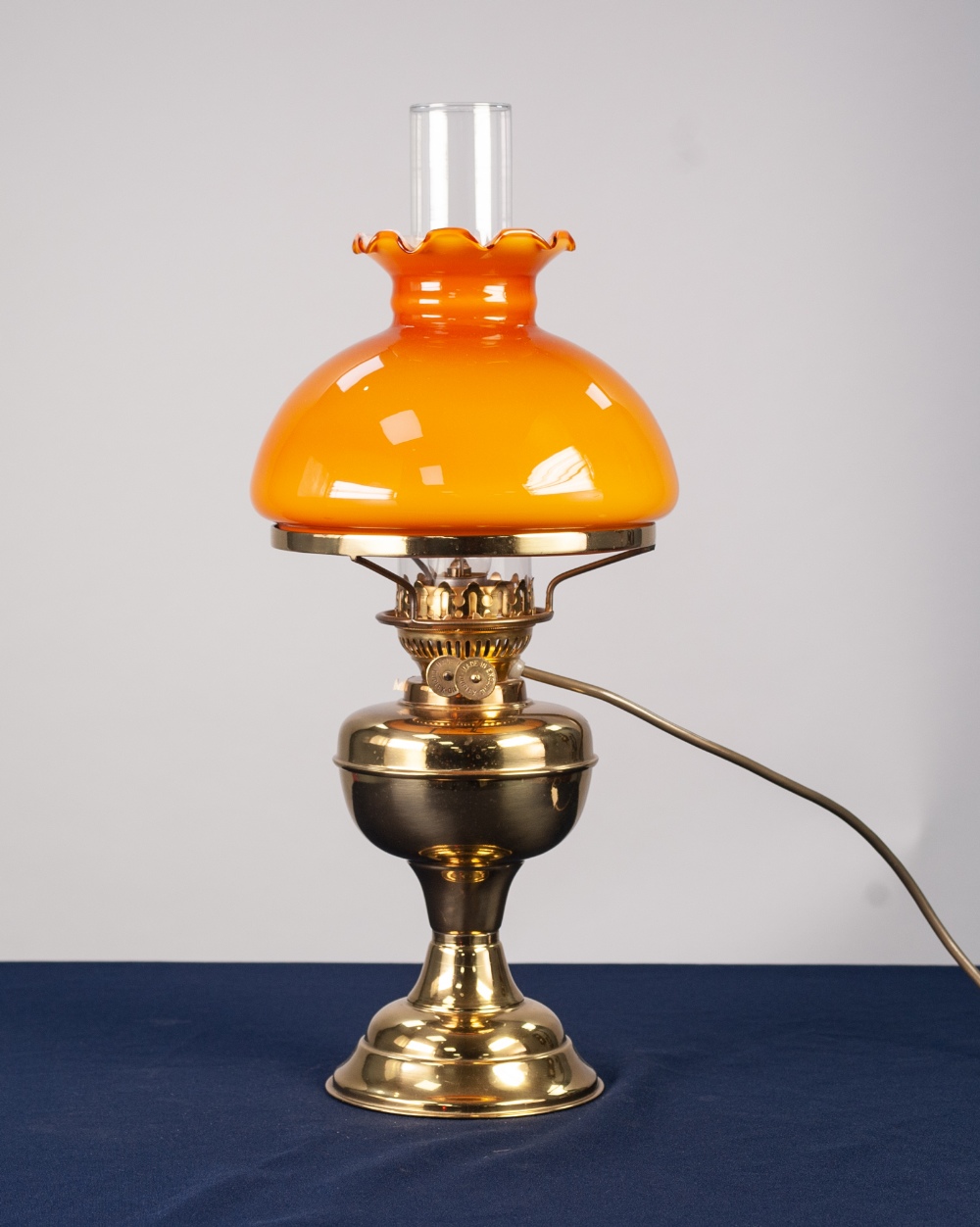 AN ADAPTED OIL LAMP WITH ORANGE GLASS GLOBE AND CLEAR GLASS FUNNEL