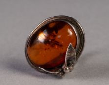 CRAFT MADE SILVER COLOURED METAL RING with a cabochon oval amber in a collet setting, with leaf