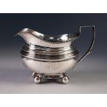 GEORGE III NEWCASTLE SILVER CREAM JUG with gadrooned rim and angular handle, standing on four ball