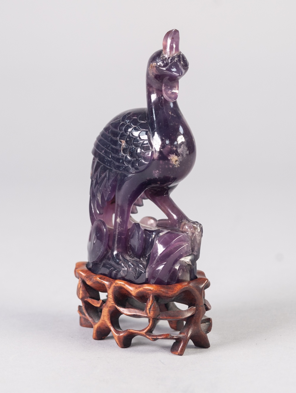 A TWENTIETH CENTURY CHINESE CARVED AMETHYST QUARTZ PHOENIX, on openwork wooden stand, 4 1/2" (11.