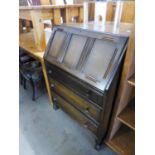 AN OAK BUREAU OF THRE LONG DRAWERS UNDER A FALL-FRONT SECTION WIT LINEN FOLD DECORATION