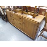 AN ERCOL ELM SIDEBOARD, WITH THREE CENTRAL DRAWERS, FLANKED BY TWO CUPBOARDS, RAISED ON CASTORS