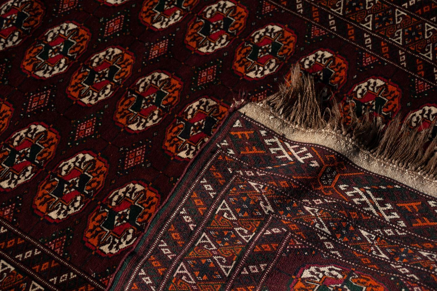 TURKOMAN BOKHARA WOOL RUG, with three rows of ten Herat Mauri primary guls on a dark wine red field, - Image 2 of 3
