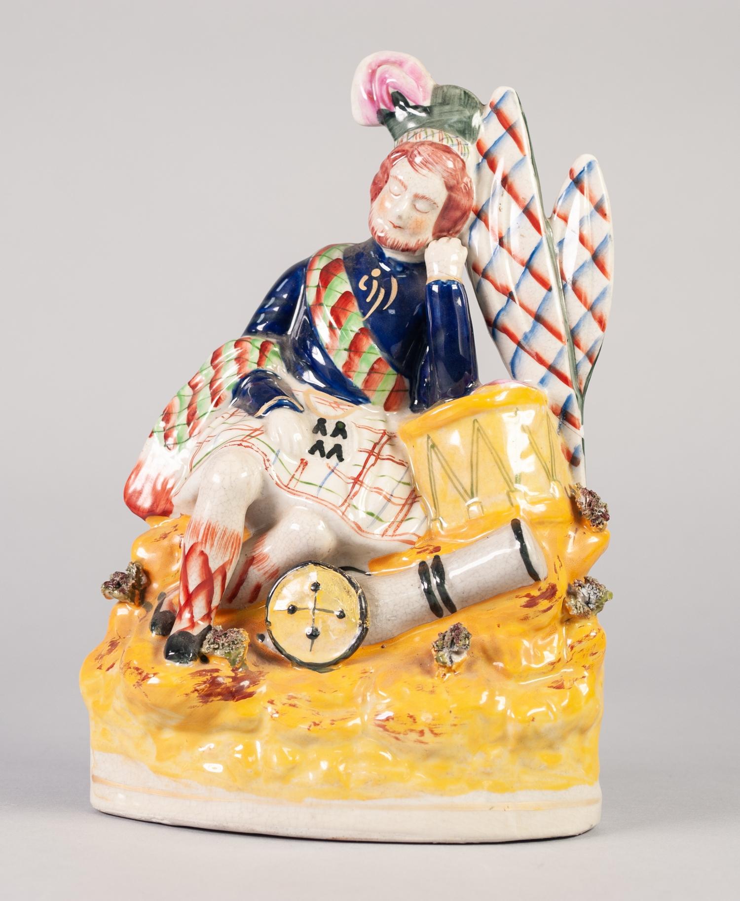 STAFFORDSHIRE POTTERY FIGURE OF A HIGHLAND SOLDIER, modelled seated against a drum, on a floral